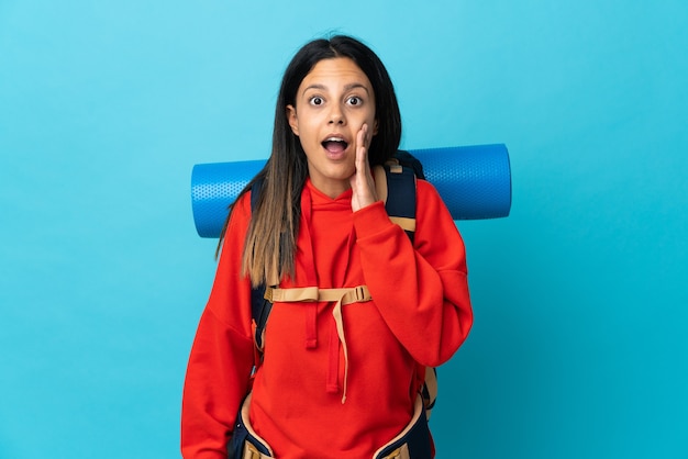 Mujer joven alpinista con mochila con sorpresa y expresión facial conmocionada