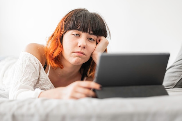 Mujer joven alternativa con cabello teñido descansando en casa y haciendo la tarea mientras sonríe y se relaja