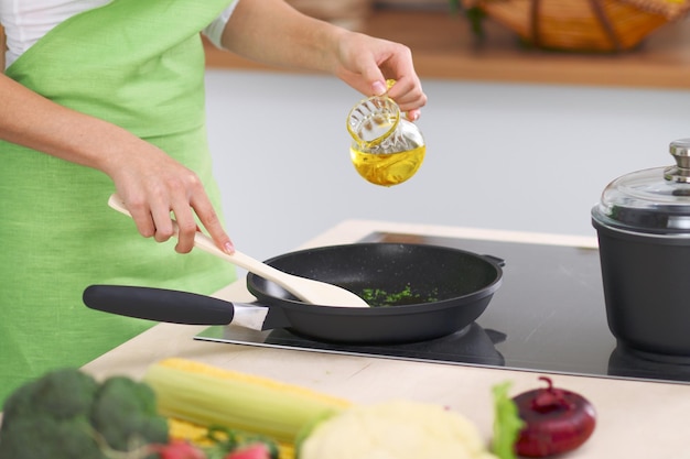 Mujer joven ama de casa cocinando en la cocina mientras agrega aceite de oliva Concepto de comida fresca y saludable en casa