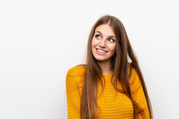 Mujer joven con amarillo sobre la pared blanca aislada que ríe y que mira para arriba