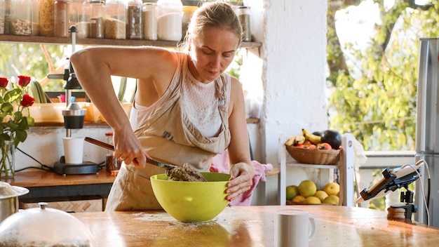 Mujer joven amasando la masa para el pan de centeno integral casero en un recipiente de plástico verde