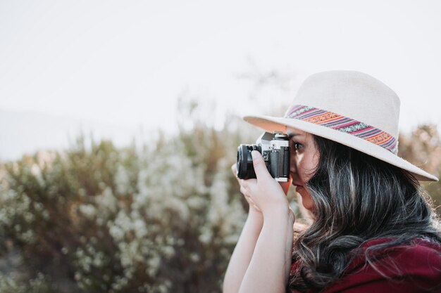 Mujer joven de ambiente de verano con un sombrero y una cámara vintage para tomar fotos en un espacio natural