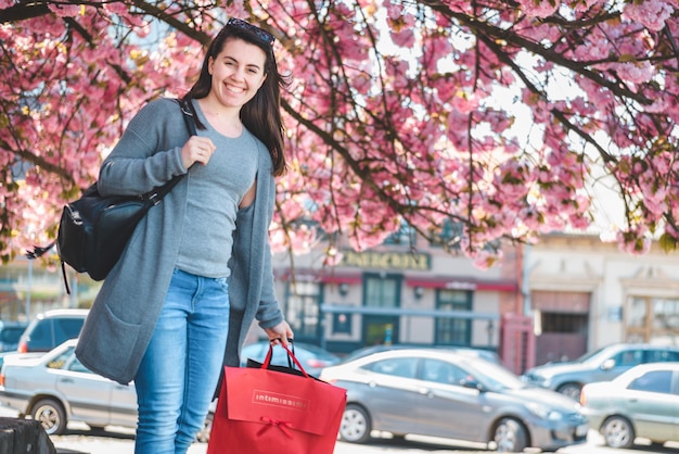 mujer joven, ambulante, por, calle, con, bolsas, florecer, sakura, en, plano de fondo