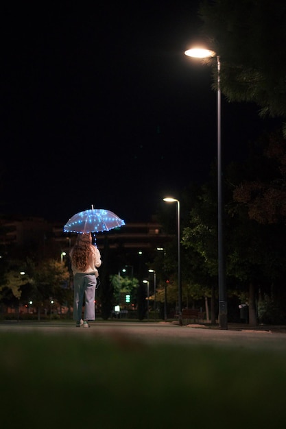 mujer joven, ambulante, con, paraguas, con, luces, por la noche