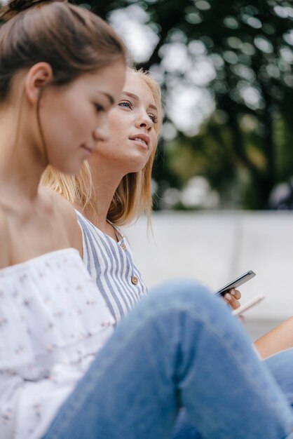 mujer joven, con, amigo, sentado, tenencia, teléfono celular