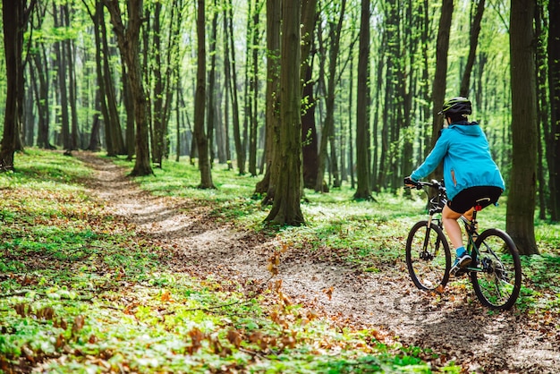 Mujer joven andar en bicicleta en el bosque por sendero