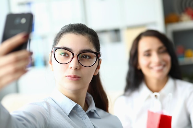 Mujer joven con anteojos sostiene el teléfono frente a la cara y sonríe a sus colegas en la oficina