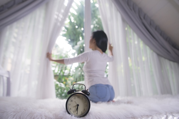 mujer joven en el apartamento moderno abriendo las cortinas de la ventana después de despertar