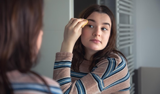 Una mujer joven aplica base en su rostro maquillaje matutino