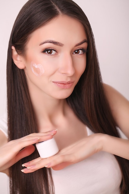 Mujer joven aplica crema hidratante en la cara