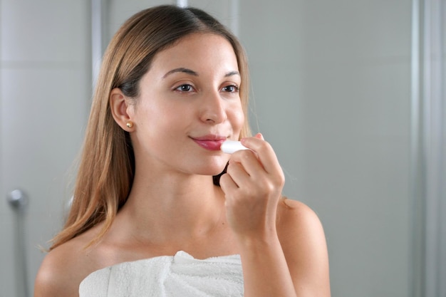 Mujer joven aplicando bálsamo labial frente al espejo interior