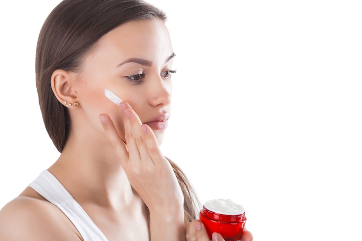 Foto mujer joven aplicando crema facial. crema suavizante facial. un frasco con crema hidratante.