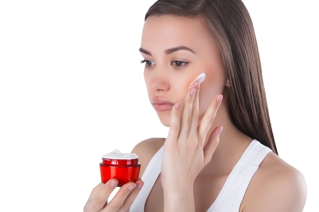 Mujer joven aplicando crema facial. Crema suavizante facial. Un frasco con crema hidratante.