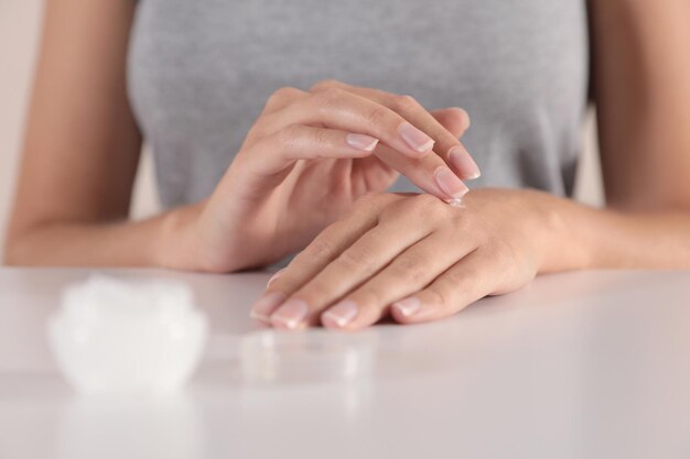 Mujer joven aplicando crema de manos en el primer plano de la mesa