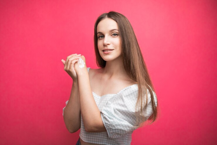 Mujer joven aplicando crema de manos sobre fondo rosa