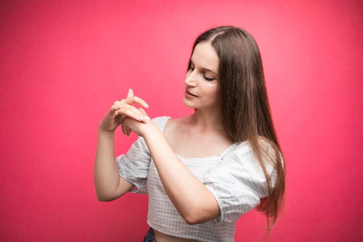 Mujer joven aplicando crema de manos sobre fondo rosa