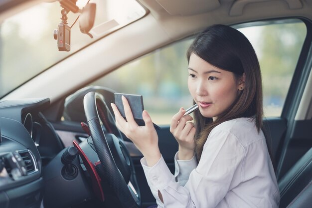 Mujer joven aplicando lápiz labial en el coche