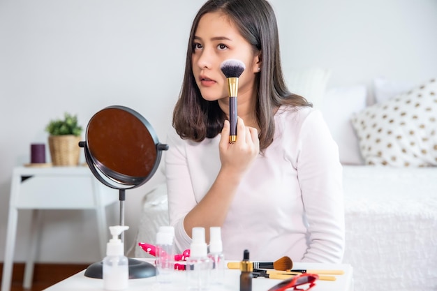 Mujer joven aplicando maquillaje en la mesa en casa