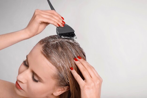 Mujer joven aplicando máscara en su cabello sobre fondo claro