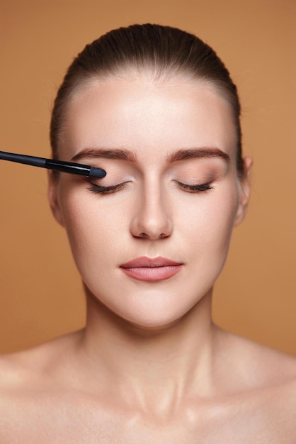 Mujer joven aplicando sombras de ojos en los párpados