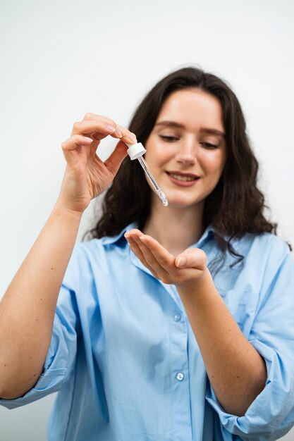 Foto mujer joven está aplicando suero hidratante en la piel de la cara chica con ácido hialurónico o pipeta de suero en las manos de primer plano