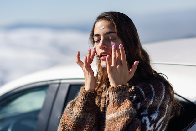 Mujer joven aplicar protector solar en la cara en el paisaje de nieve