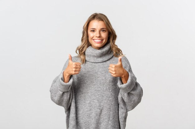 Mujer joven de apoyo con pelo corto rubio, mostrando el pulgar hacia arriba y sonriendo, como algo o dar