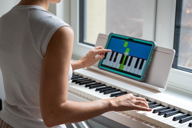 Mujer joven aprendiendo a tocar el teclado en casa usando una aplicación interactiva usando aplicaciones móviles para