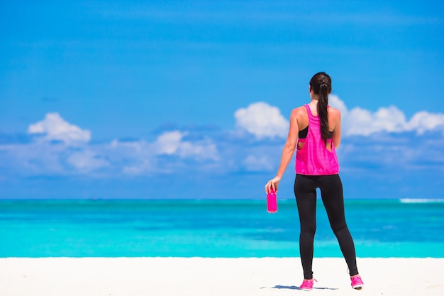 Mujer joven apta que hace ejercicios en la playa blanca tropical en su ropa de deportes