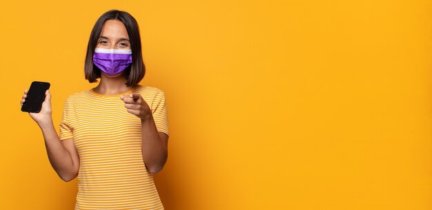 Mujer joven apuntando a la cámara con una sonrisa satisfecha, confiada y amistosa, eligiéndote