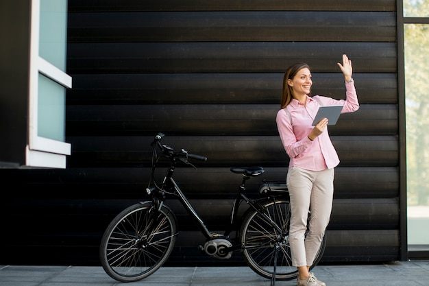 Mujer joven con archivos en las manos de pie al aire libre junto a la bicicleta eléctrica