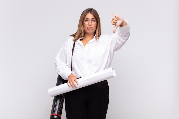 Mujer joven arquitecta que se siente enfadada, enojada, molesta, decepcionada o disgustada, mostrando los pulgares hacia abajo con una mirada seria