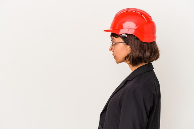 Mujer joven arquitecto con casco rojo aislado sobre fondo blanco mirando a la izquierda, pose de lado.