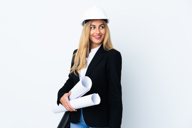 Mujer joven arquitecto con casco y sosteniendo planos sobre risa blanca aislada