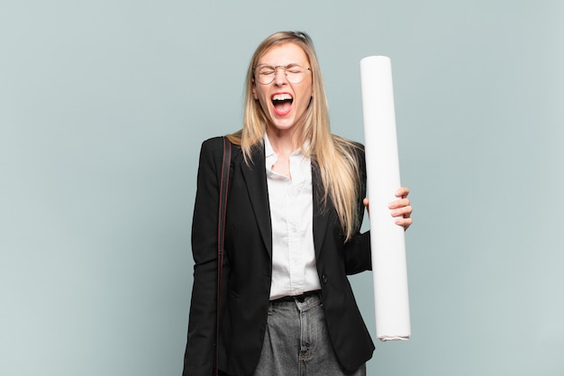 Mujer joven arquitecto gritando agresivamente, luciendo muy enojado, frustrado, indignado o molesto, gritando no