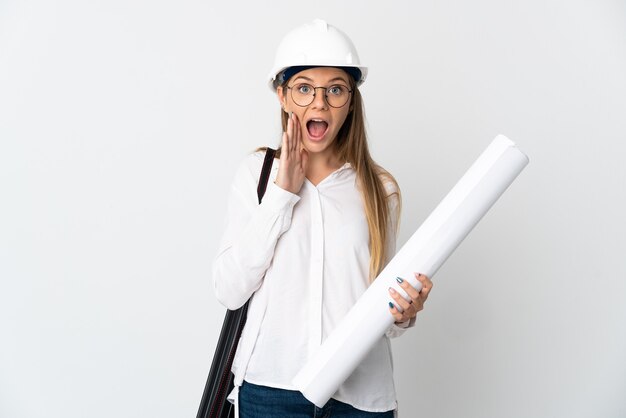 Mujer joven arquitecto lituano con casco y sosteniendo planos aislados en la pared blanca con sorpresa y expresión facial conmocionada