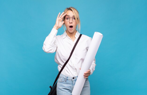 Mujer joven arquitecto mirando feliz, asombrado y sorprendido, sonriendo y dándose cuenta de buenas noticias increíbles e increíbles