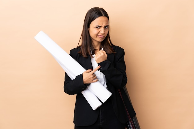 Mujer joven arquitecto sosteniendo planos sobre aislados haciendo el gesto de llegar tarde