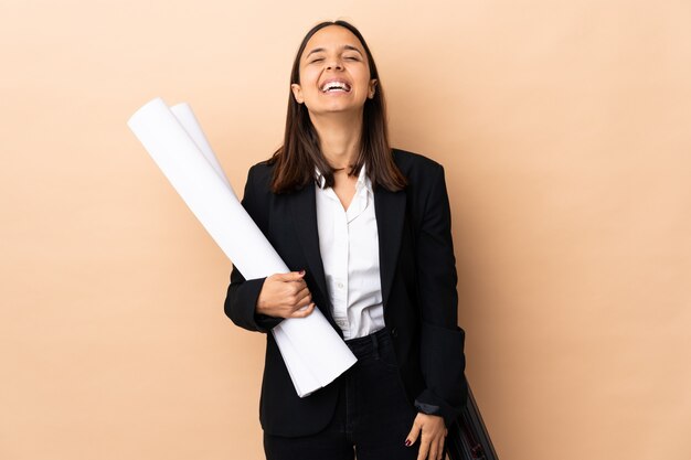 Mujer joven arquitecto sosteniendo planos sobre fondo aislado riendo