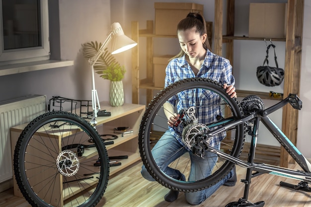 Mujer joven arreglando una bicicleta de montaña en un taller. Concepto de preparación para la nueva temporada, reparación y mantenimiento.