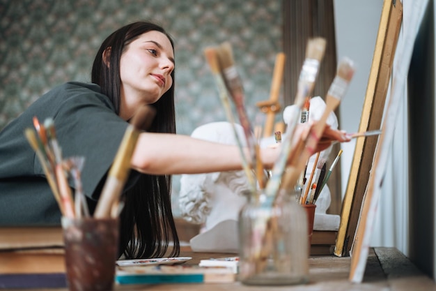 Mujer joven artista adolescente chica estudiante con cabello largo oscuro en casual dibuja imagen en el estudio de arte