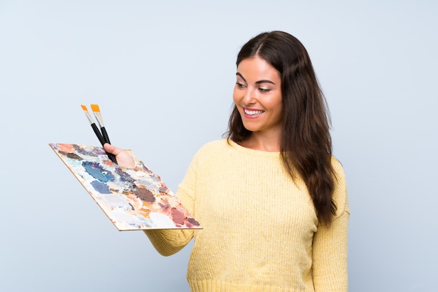 Mujer joven artista sobre pared azul aislada con expresión feliz