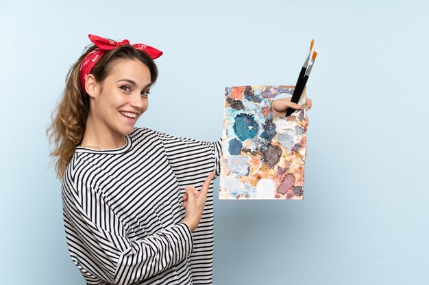 Mujer joven artista sosteniendo una paleta y apuntando