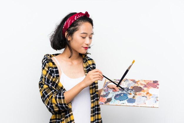 Mujer joven artista sosteniendo una paleta sobre pared blanca aislada