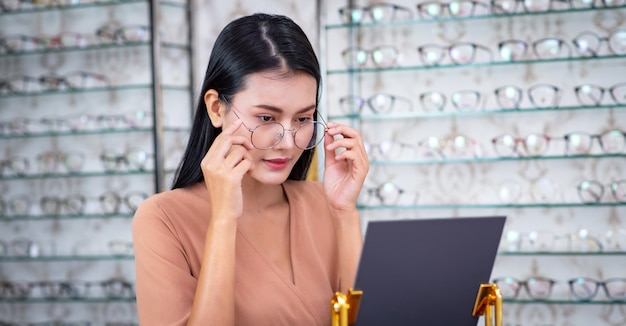 La mujer joven Asia está eligiendo vidrios en tienda óptica.