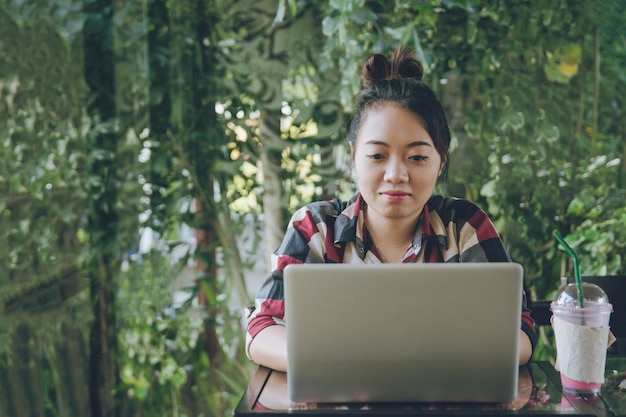 Mujer joven de Asia que se sienta solamente en la cafetería que trabaja en una computadora portátil