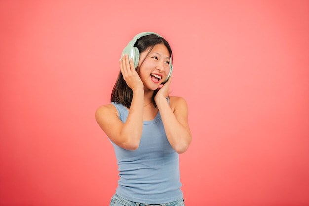 Mujer joven asiática bailando música usando auriculares inalámbricos y una aplicación de teléfono móvil en rojo