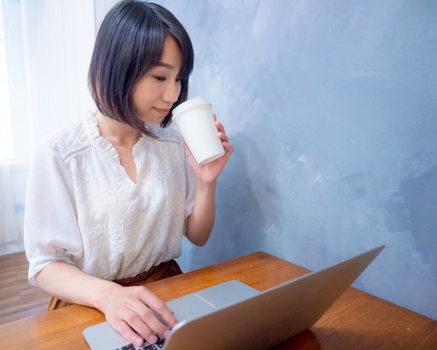 Mujer joven asiática bebe delante de la computadora portátil