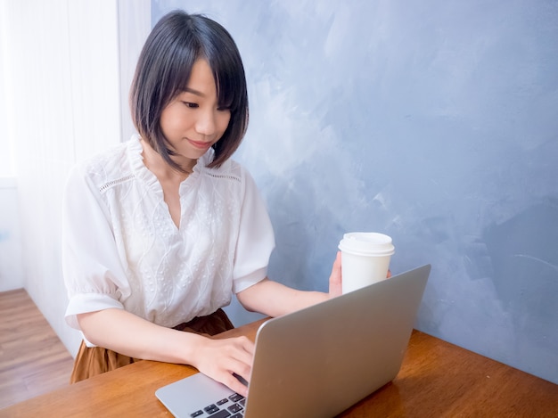 Mujer joven asiática bebe delante de la computadora portátil