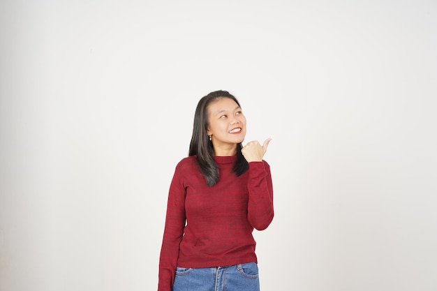 Mujer joven asiática con camiseta roja apuntando hacia el espacio de copia con el pulgar aislado sobre un fondo blanco